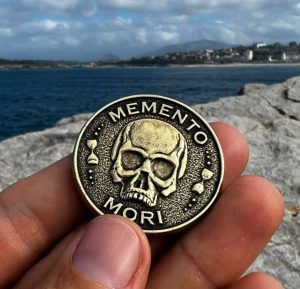Moneda Memento Mori con una calavera sostenida entre los dedos