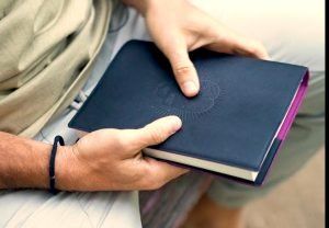 Manos sujetando un diario de tapa azul para el examen de la noche